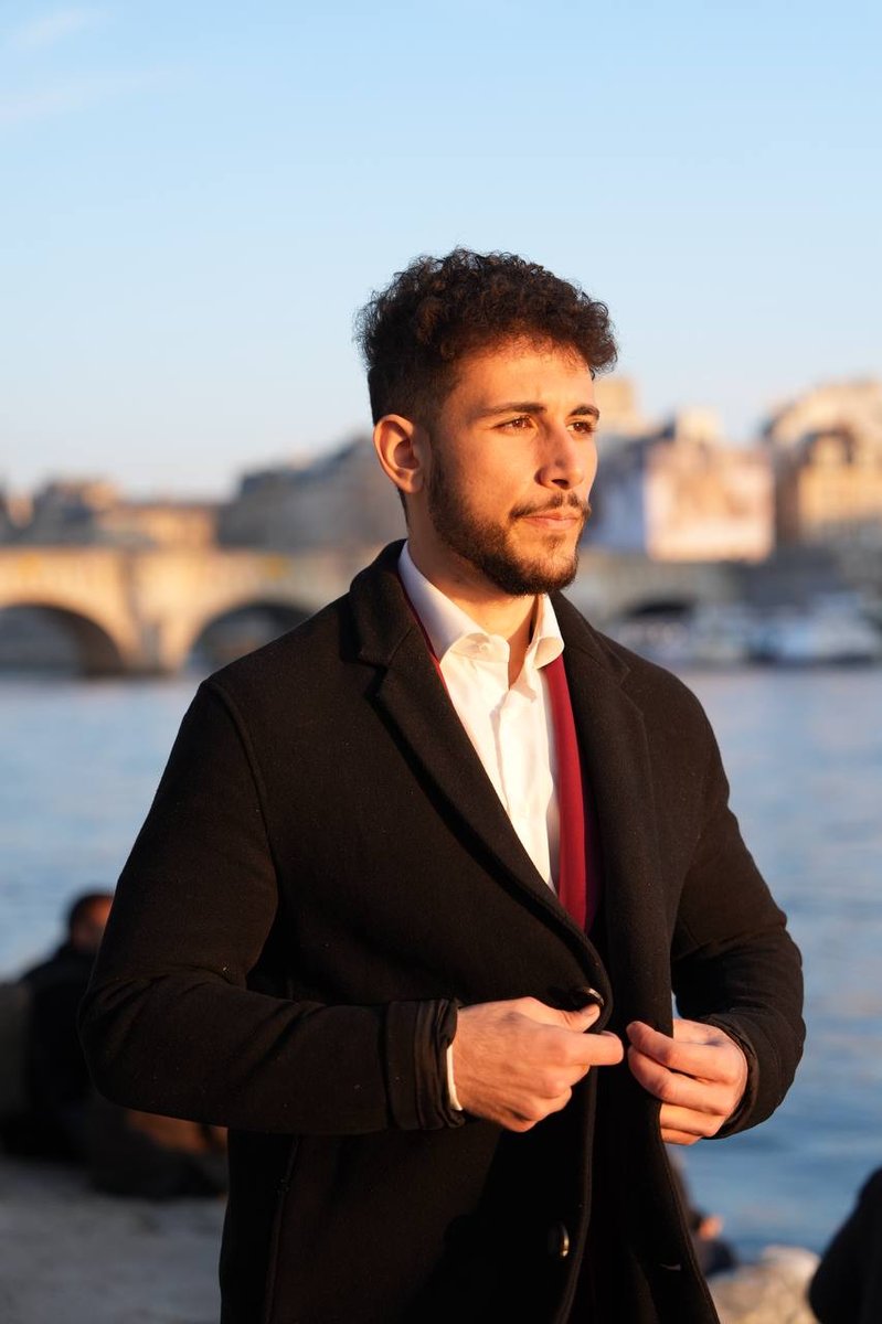El Rayhan Loudhni sur les quais de Seine à Paris, manteau noir et pont en arrière-plan